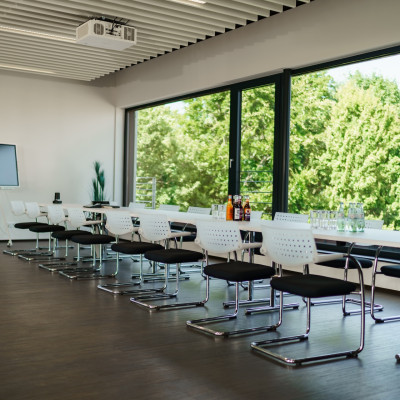 Blockbestuhlung vor einer großen Fensterfront mit Aussicht auf grüne Laubbäume.