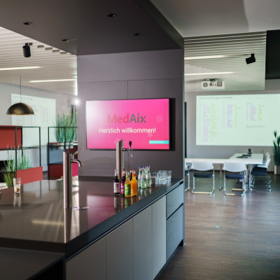 Küche mit Insel im Tagungsraum Rooftop57 mit Wasserspender, Getränkeflaschen und einen Bildschirm.